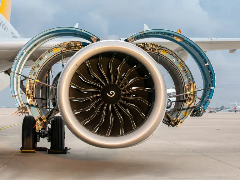 Jet engine of a modern commercial aircraft with nacelle covers open for maintenance on airport apron. Detailed view of turbofan engine and landing gear in daylight.