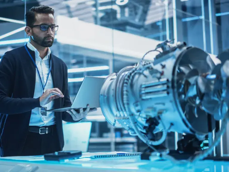 Young Industrial Engineer Working on a Futuristic Jet Engine, Standing with Laptop Computer in Scientific Technology Lab. Scientist Developing a New Electric Motor in a Research Facility